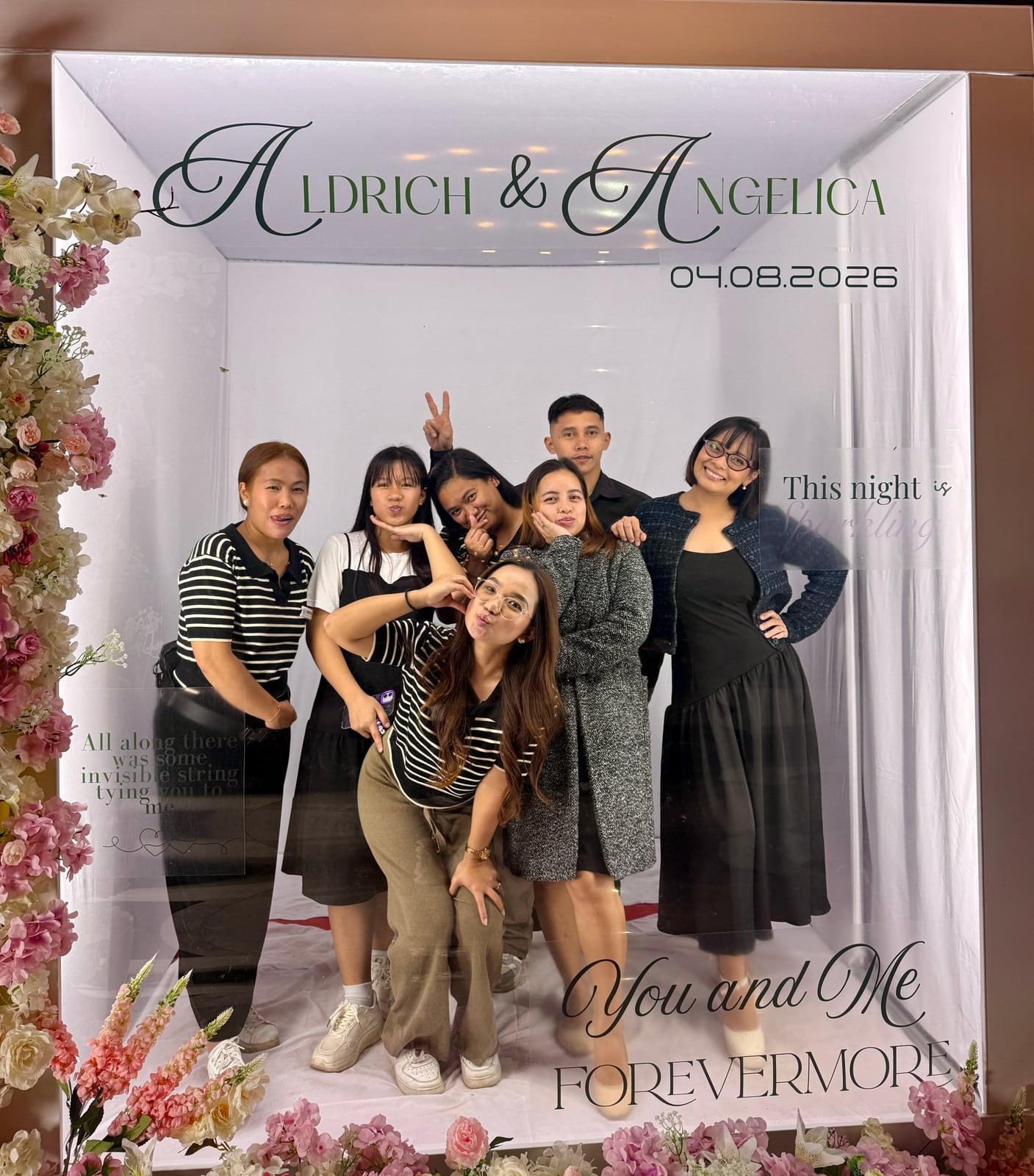 The team posing together in a wedding photo booth backdrop reading Aldrich and Angelica